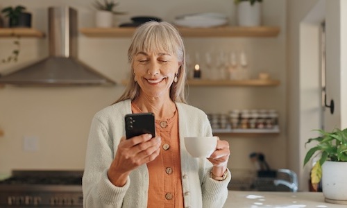 a woman smiling, holding a phone and a cup