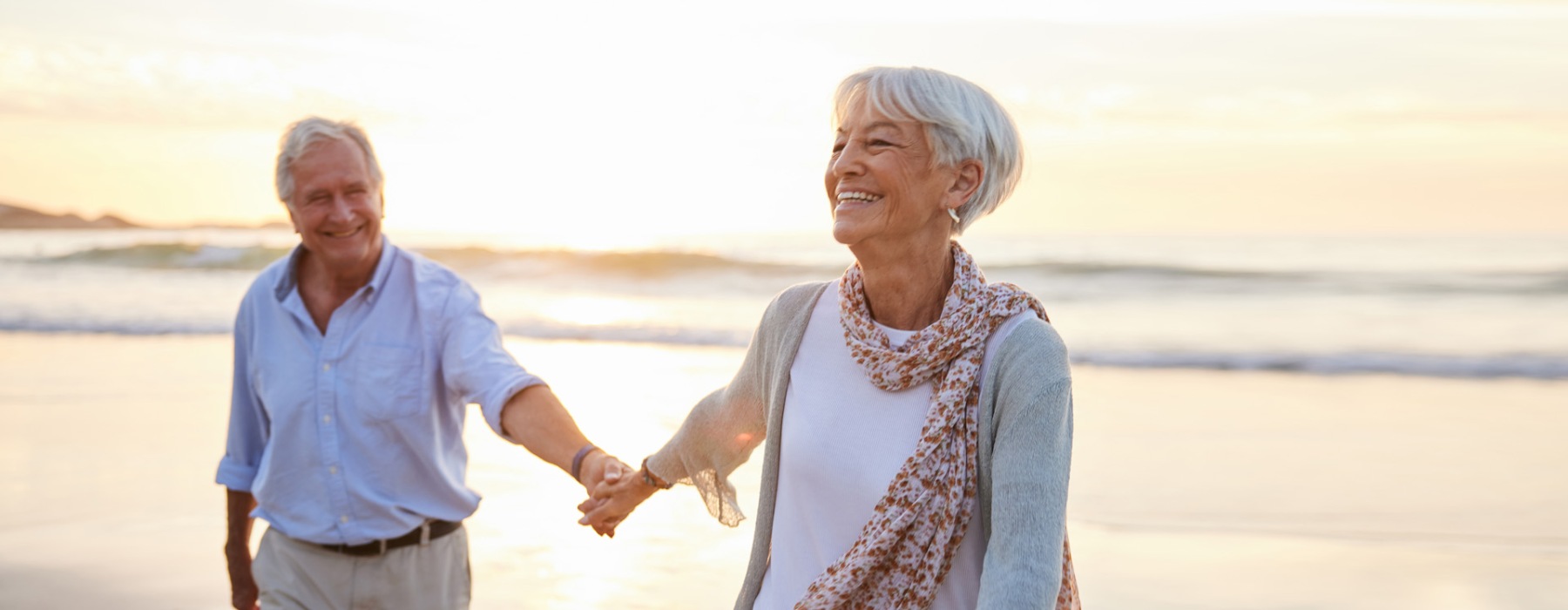 Senior couple holding hands while walking on the beach and sunset and laughing